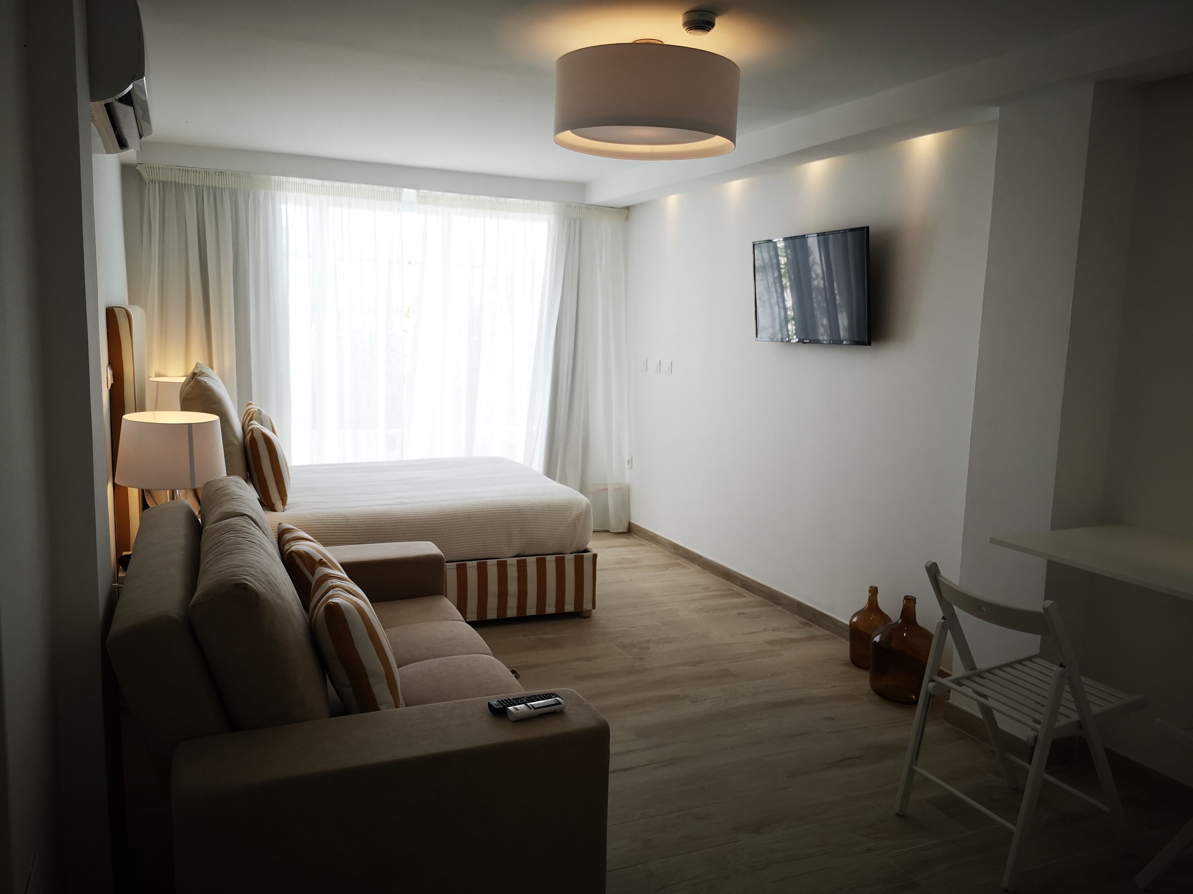 Quarto de hotel moderno com cama, sofá, escrivaninha e televisão.