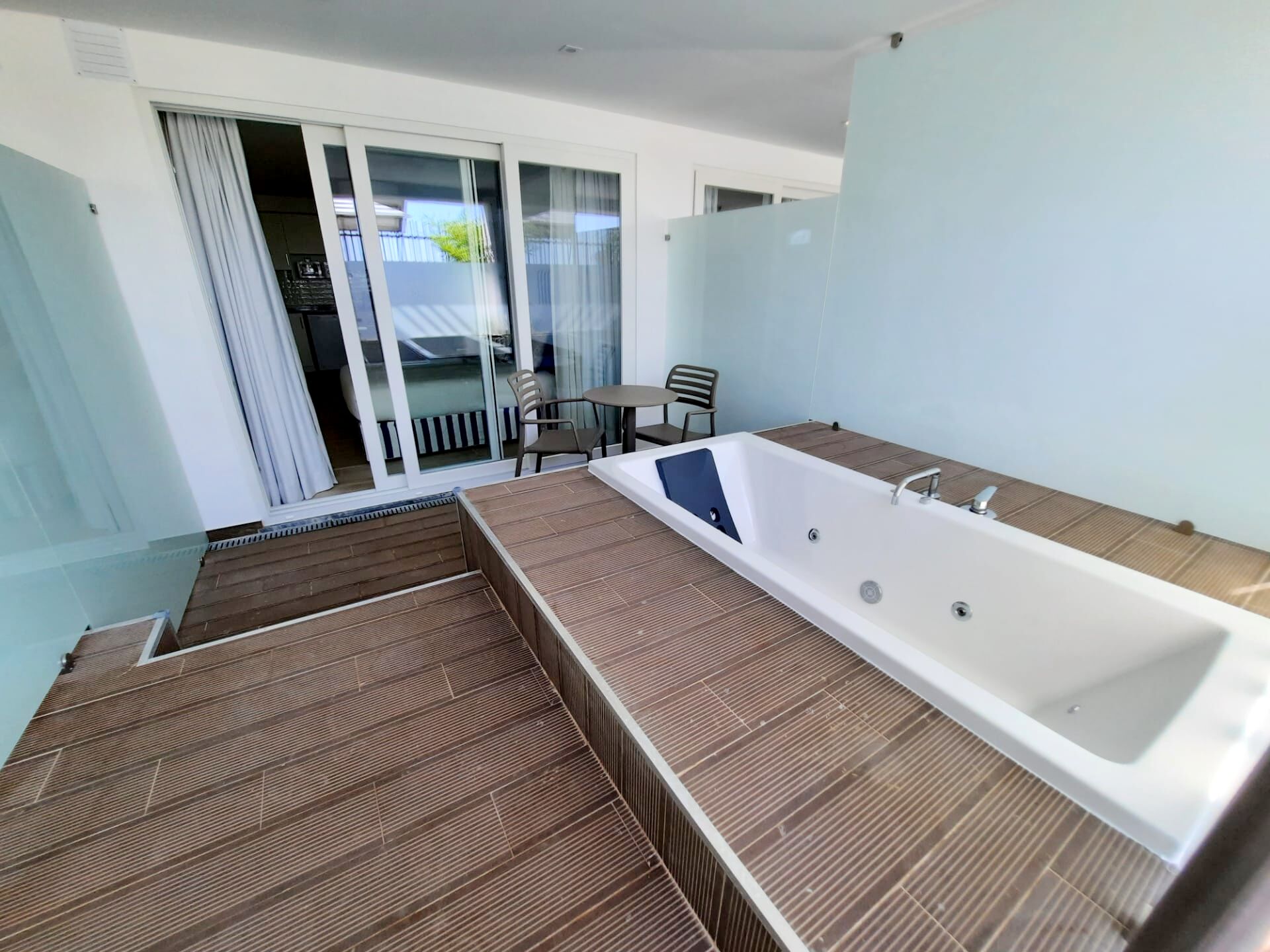 A modern bathroom with a large bathtub, a shower area, and a small seating area with chairs and a table.