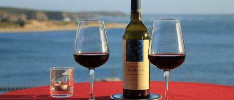 A bottle of Chaminé wine, two wine glasses, and a small candle on a red table by the sea.