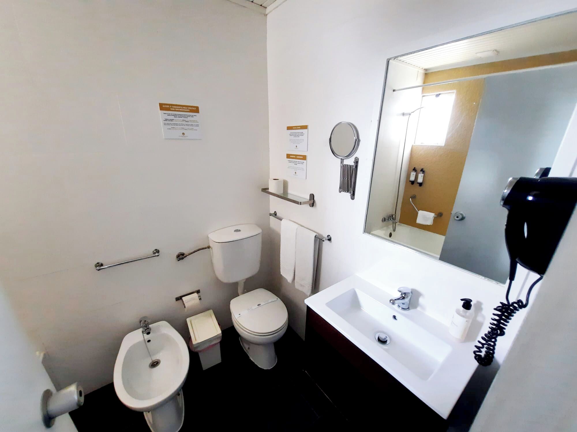 Ein kleines Hotelbad mit Toilette, Bidet, Waschbecken und einem großen Spiegel.
