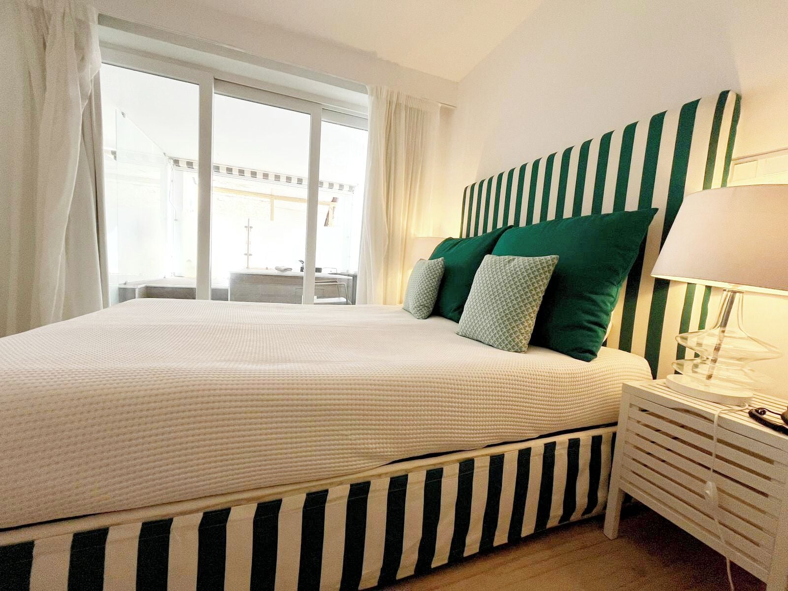 Un dormitorio con una cama grande, cabecera a rayas y una mesita de noche con lámpara.