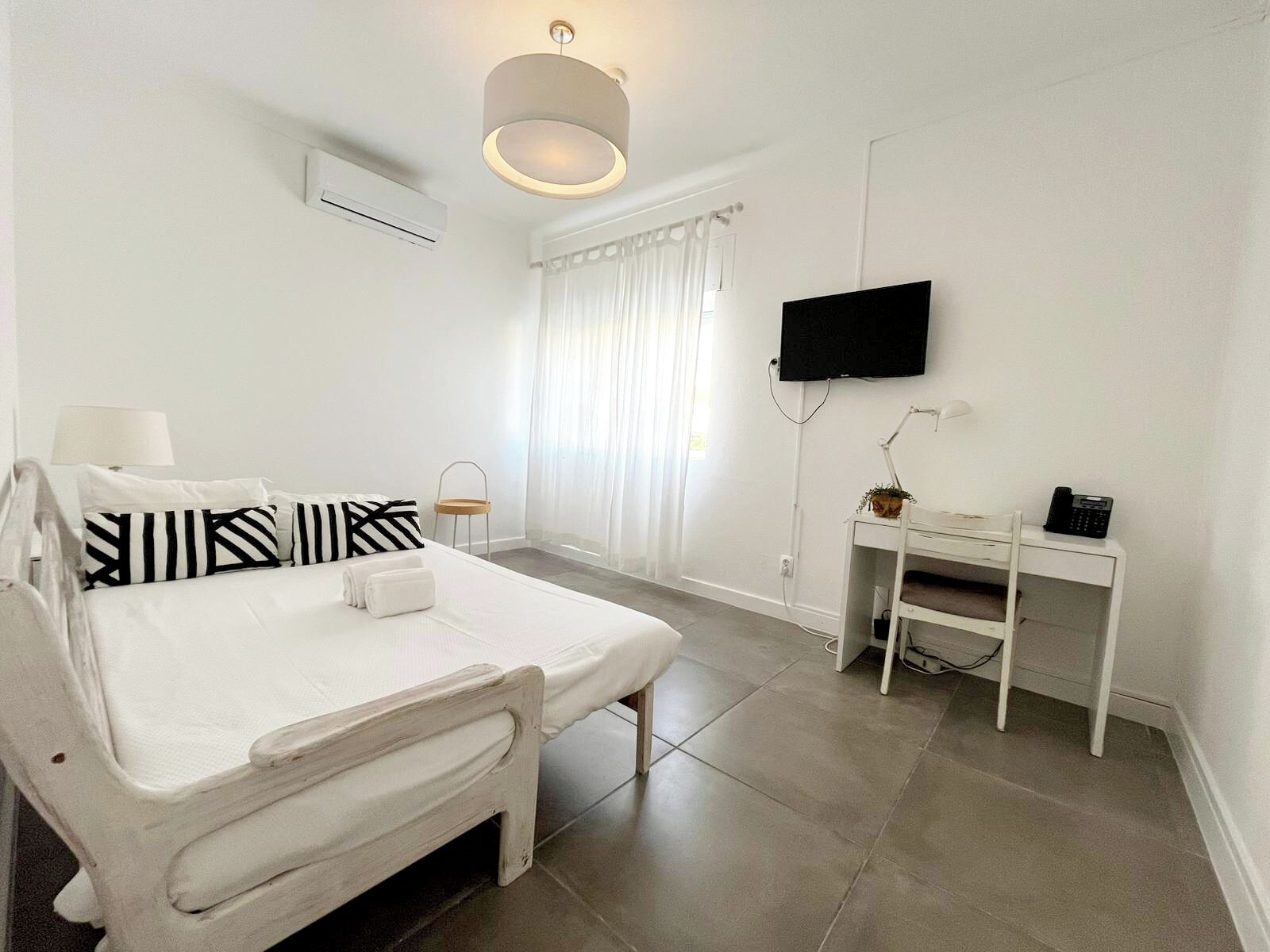 A white room with a bed, a desk, a TV, and a lamp.