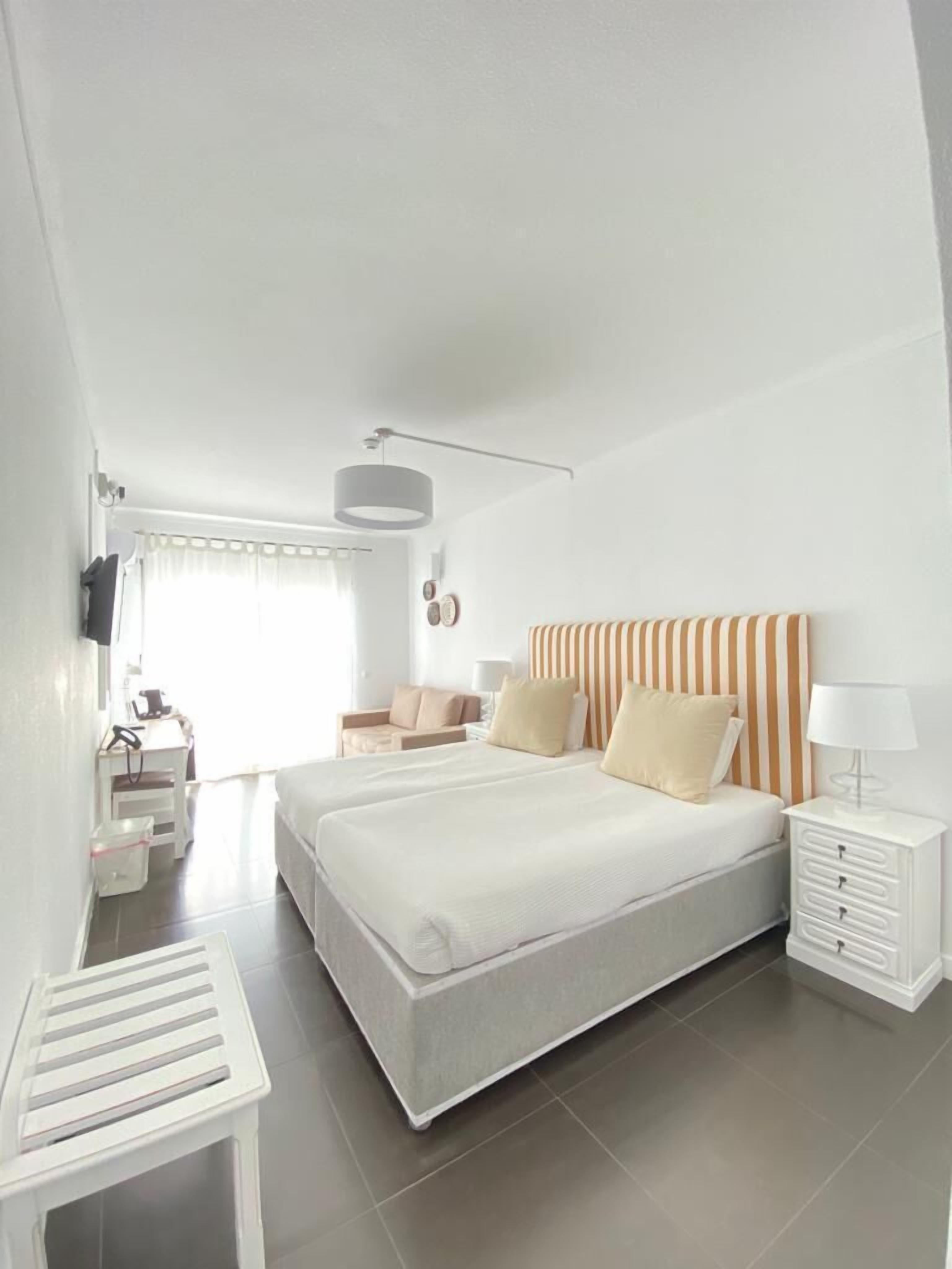 A modern bedroom with a large bed, bedside tables, a desk, and a chair.