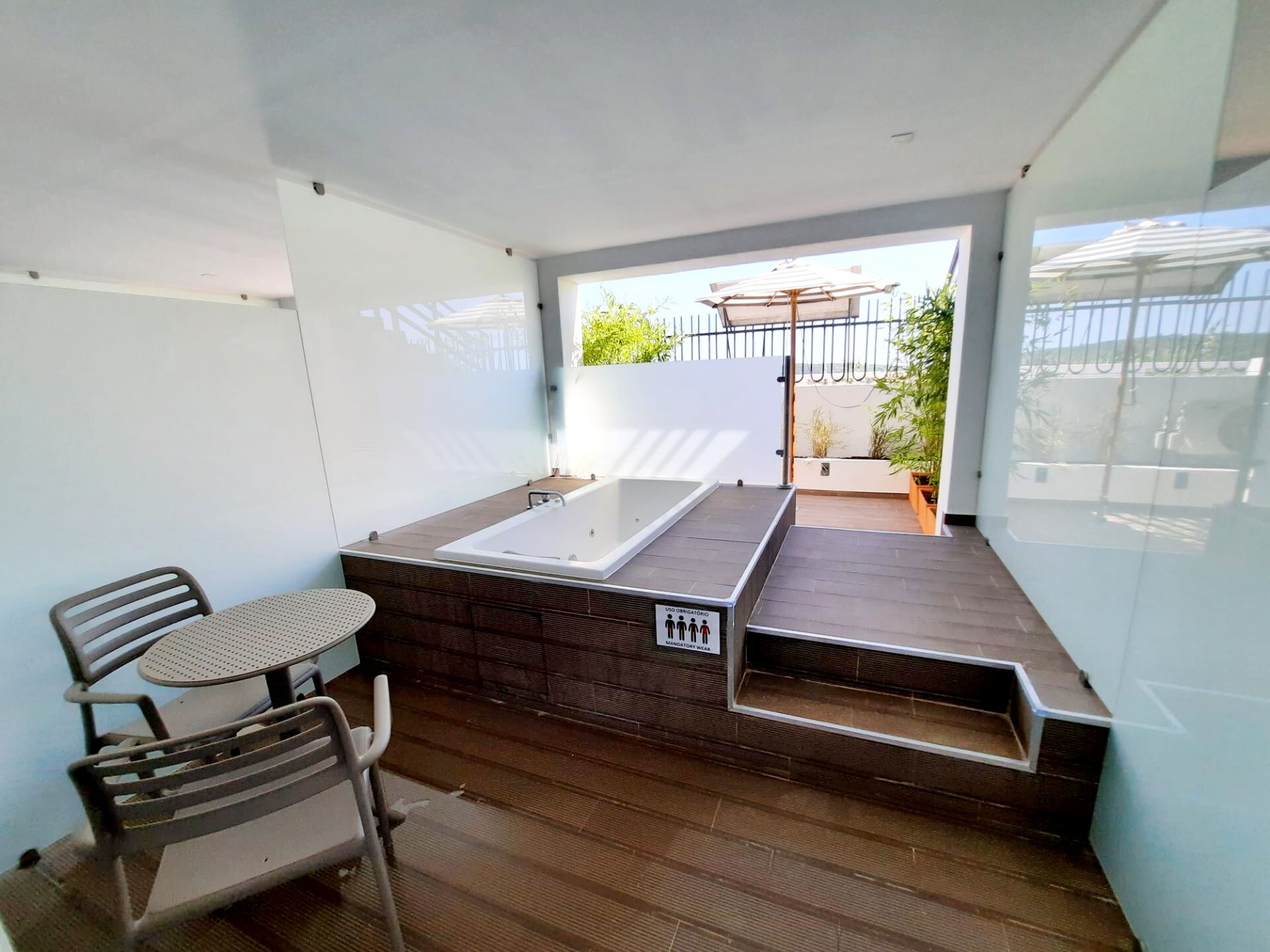 A modern outdoor bathroom with a large bathtub, a small table, and two chairs.