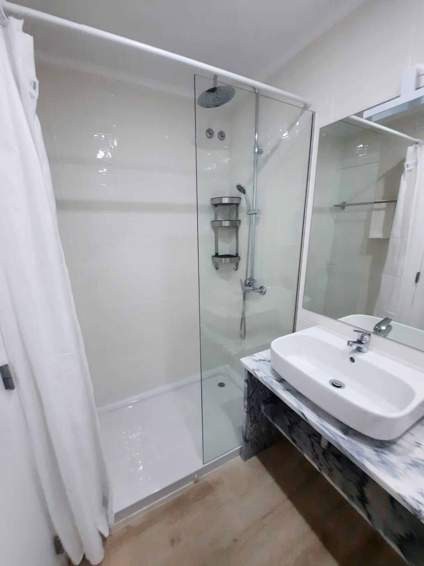 A modern bathroom with a glass-enclosed shower, a white sink, and a marble countertop.