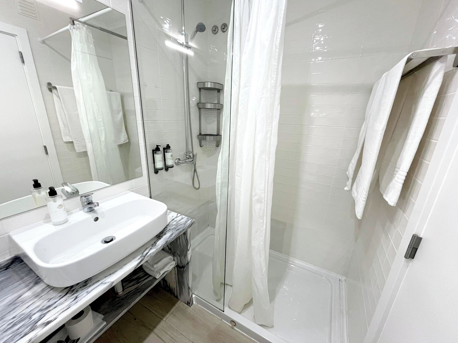 A modern bathroom with a white sink, mirror, and shower.