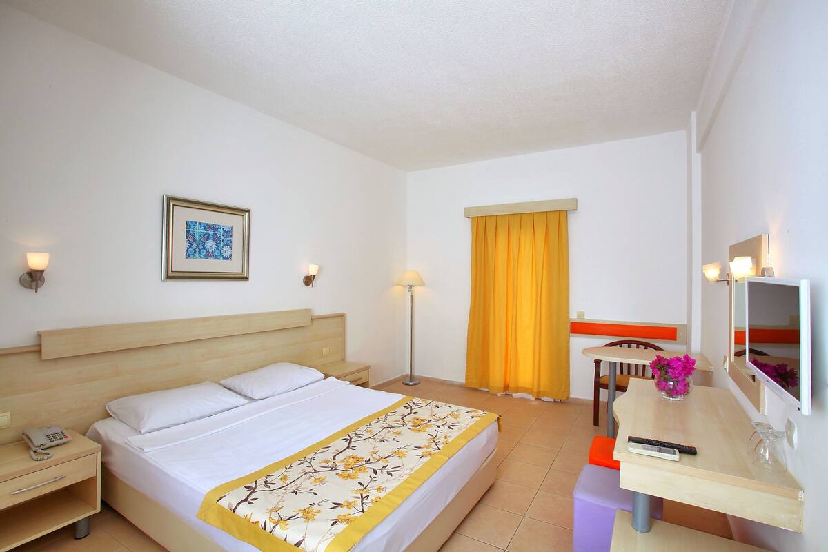 A hotel room with a bed, bedside table, lamp, desk, chair, and a mirror.