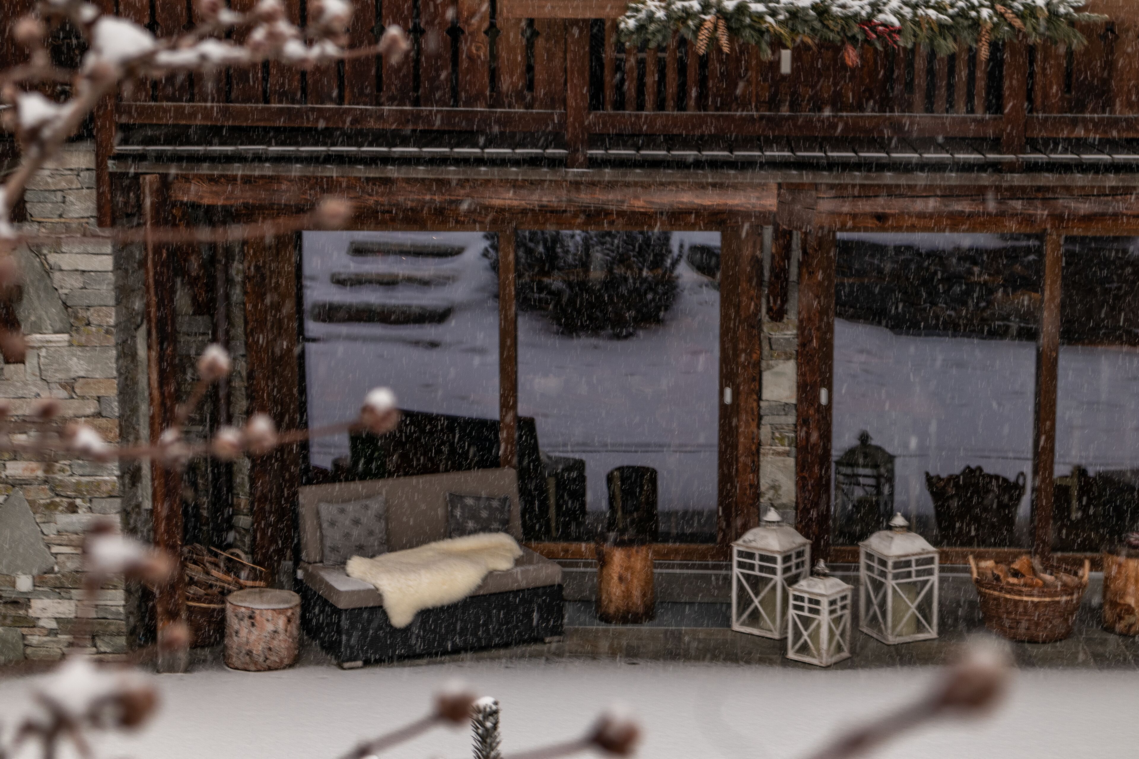 A cozy cabin with a stone exterior, a wooden balcony, and a seating area with a sofa and cushions.