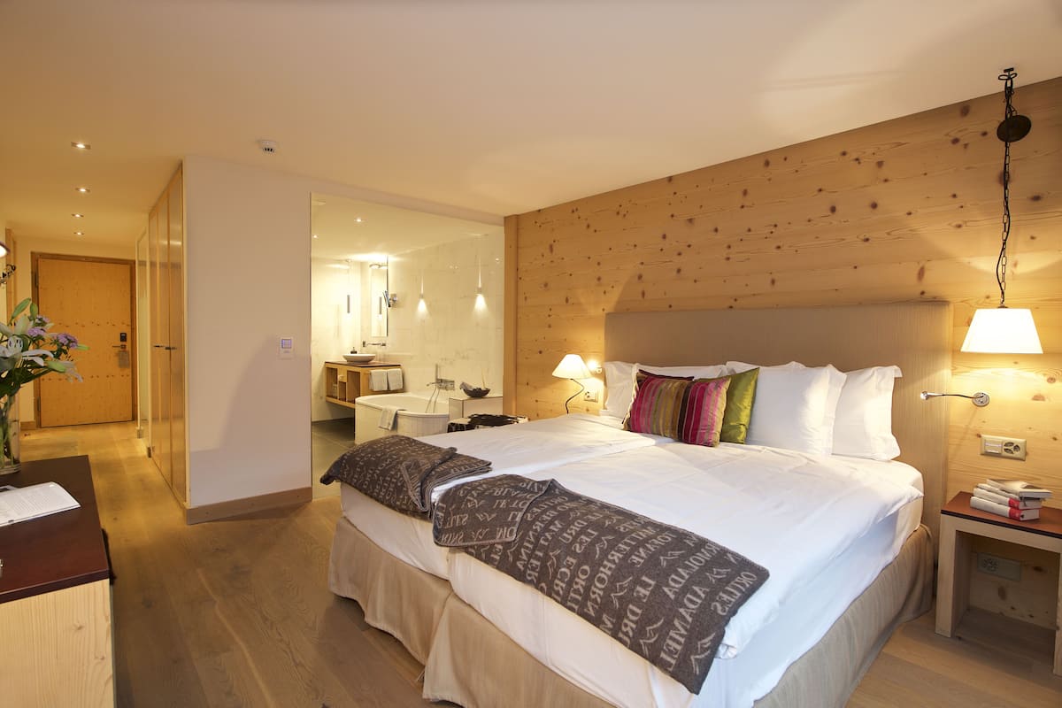 Habitación de hotel con una cama grande, mesitas de noche, cabecera de madera y un baño visible a través de una puerta abierta.