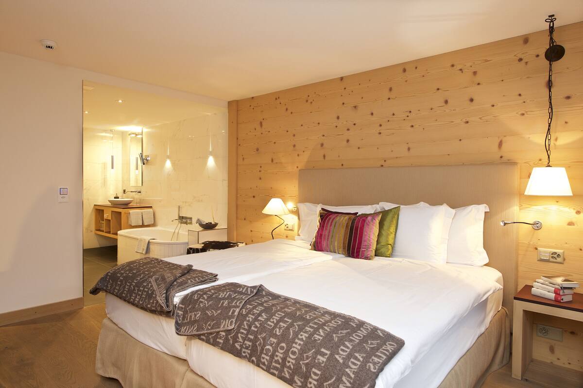 Habitación de hotel con una cama grande, cabecera de madera, lámparas de noche y un baño visible a través de una puerta abierta.
