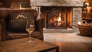 A cozy interior with a fireplace, leather seating, and a glass of wine on a table.