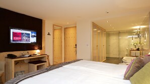 A hotel room with a bed, a desk, a television, and a bathroom with a glass shower.