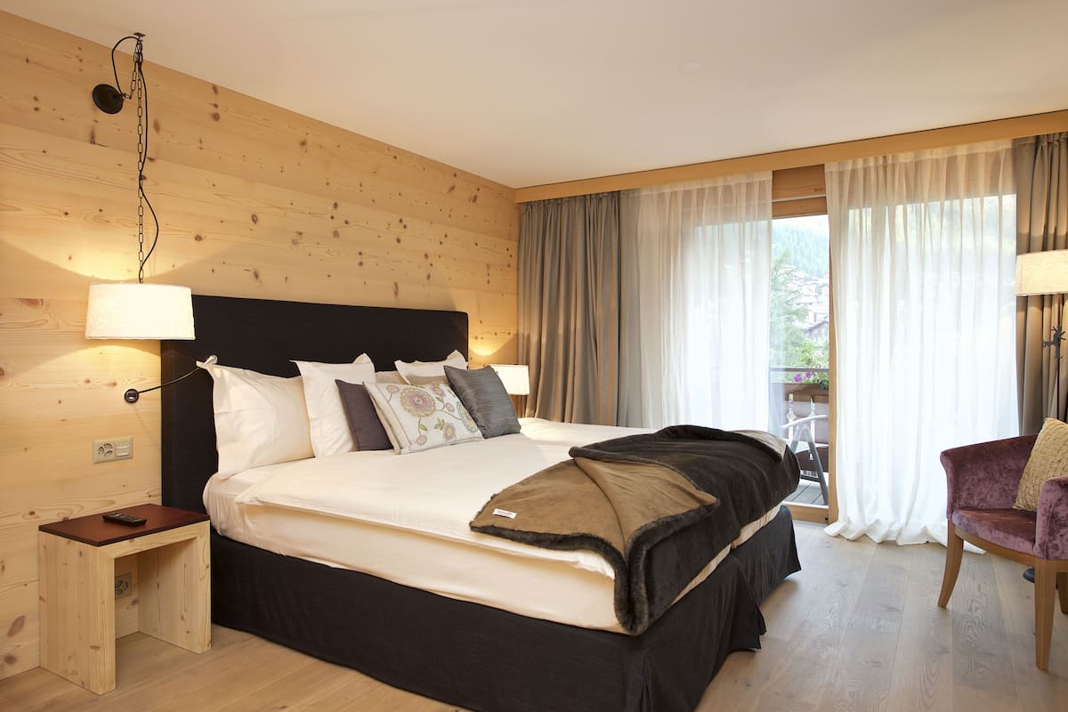 Un dormitorio con una cama grande, paredes de madera, una mesita de noche pequeña, una silla y un balcón con cortinas.