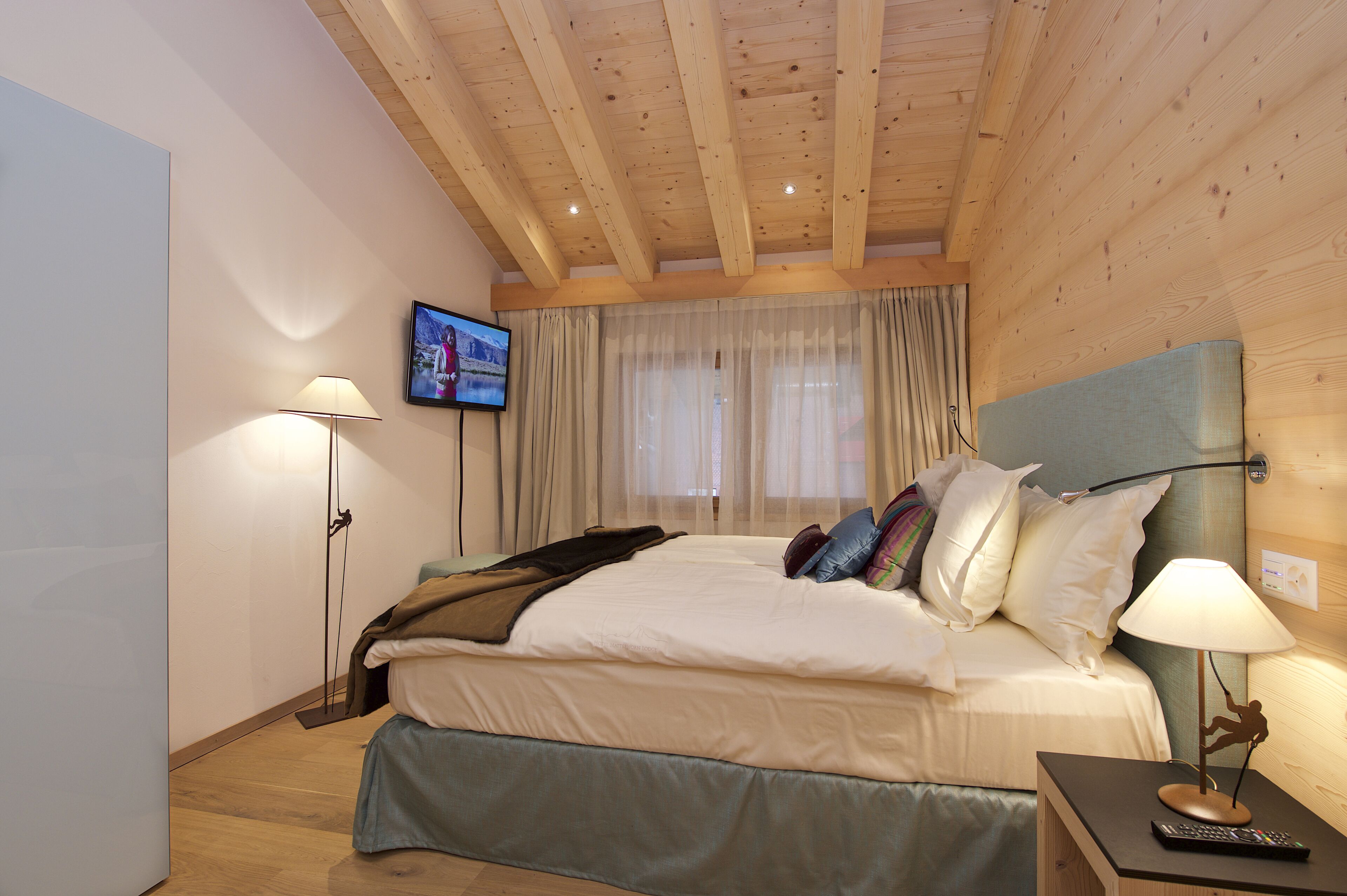 Une chambre à coucher avec un lit, un téléviseur fixé au mur et une table de chevet avec une lampe.