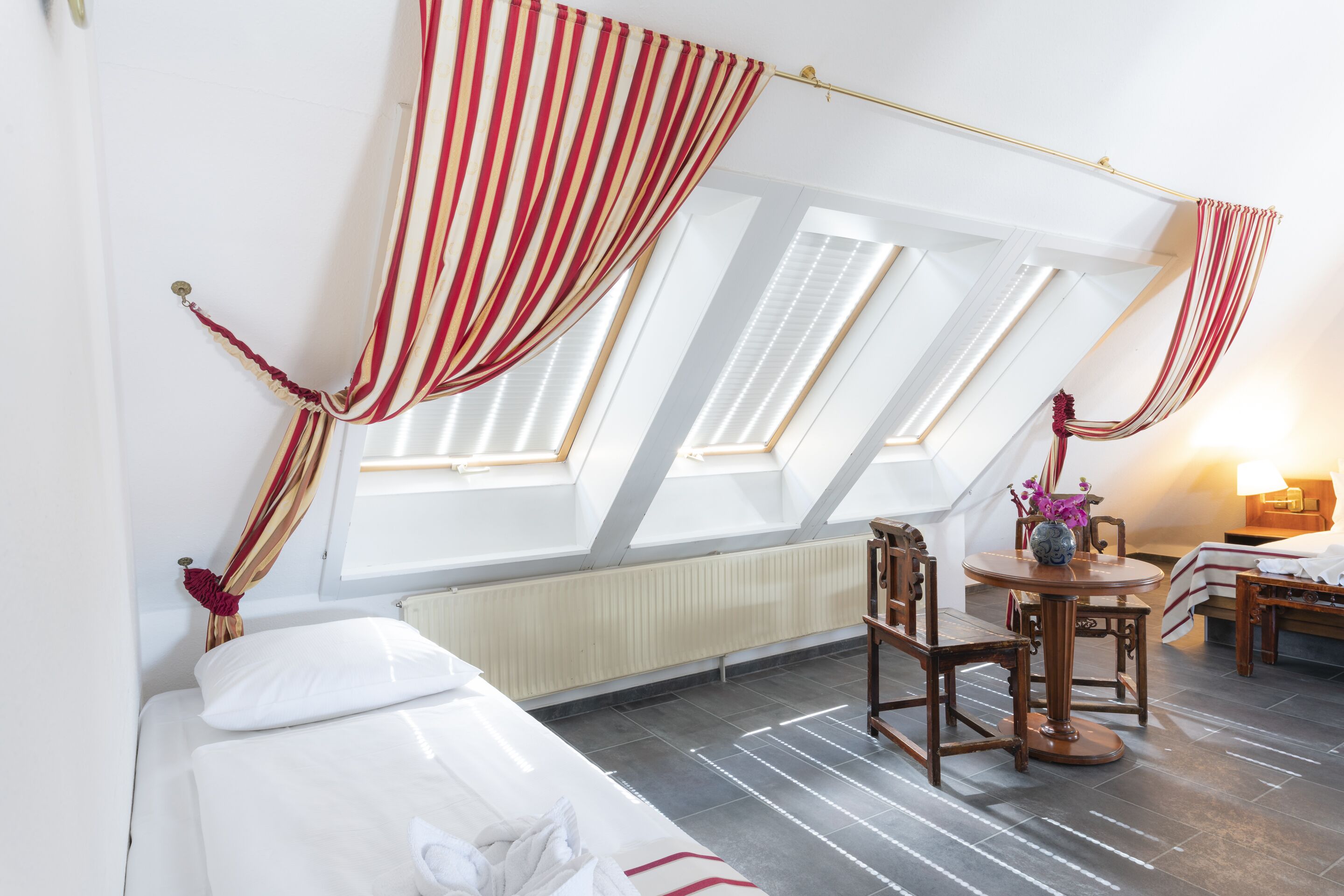 Una habitación con cama, una mesa con sillas y un ventanal con cortinas.