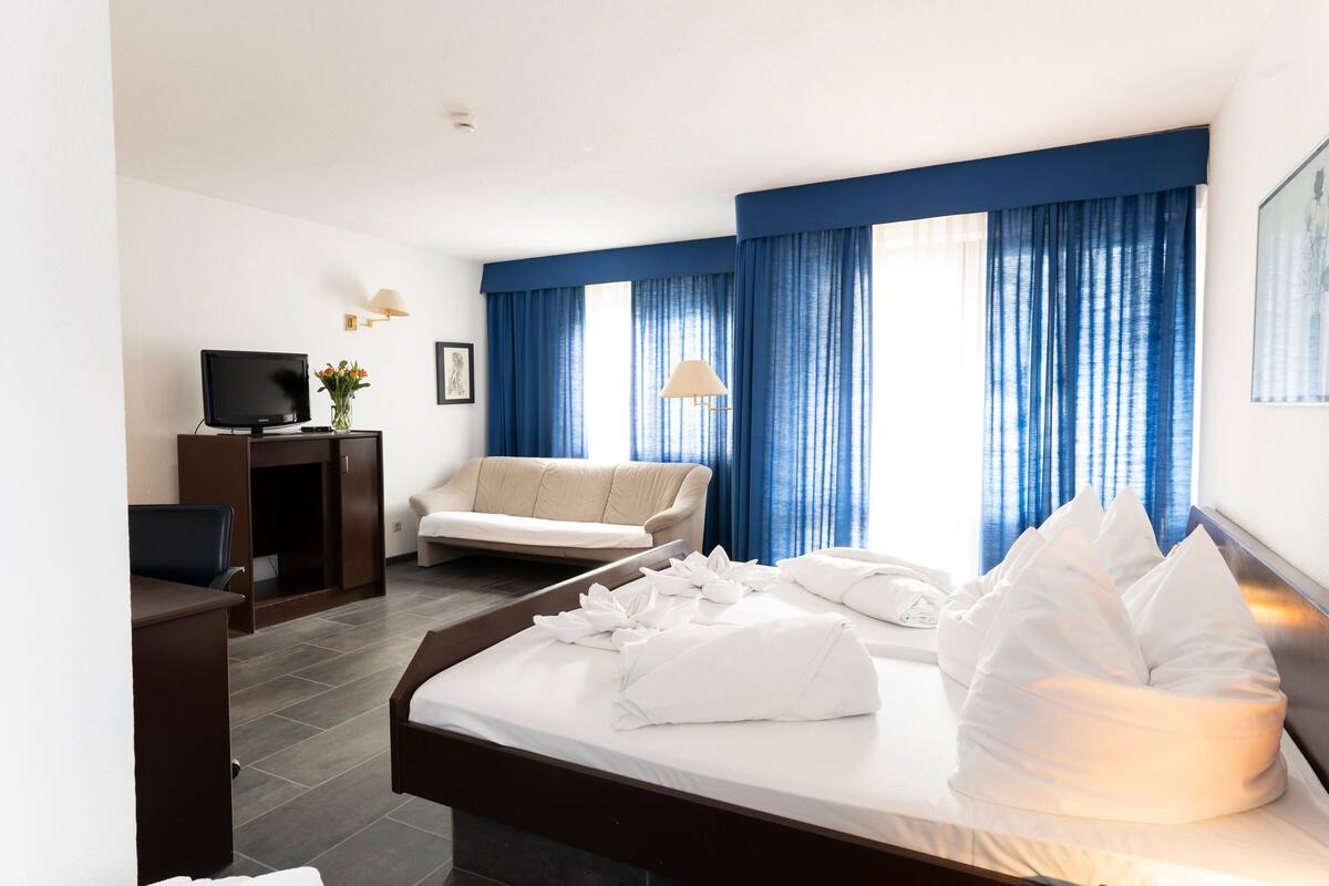 A hotel room with a bed, a desk with a computer, a sofa, and a TV.