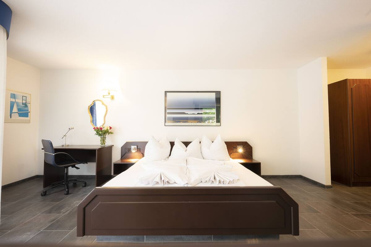 A hotel room with a bed, desk, chair, and a painting on the wall.