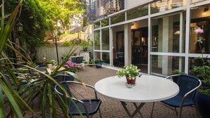 An outdoor patio area with a round table and chairs, surrounded by potted plants and a glass-enclosed building. - Hotel Astoria am Urachplatz (Stuttgart)