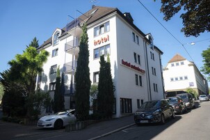 Et hotel med hvid facade, flere vinduer og en balkon.