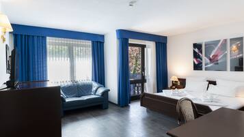 Habitació d'hotel amb un sofà blau, un llit, un escriptori i una cadira. Hi ha una finestra amb cortines blaves i una porta que dona a una zona exterior.