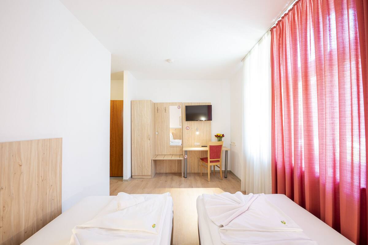 A hotel room with two beds, a desk, a chair, and a TV.