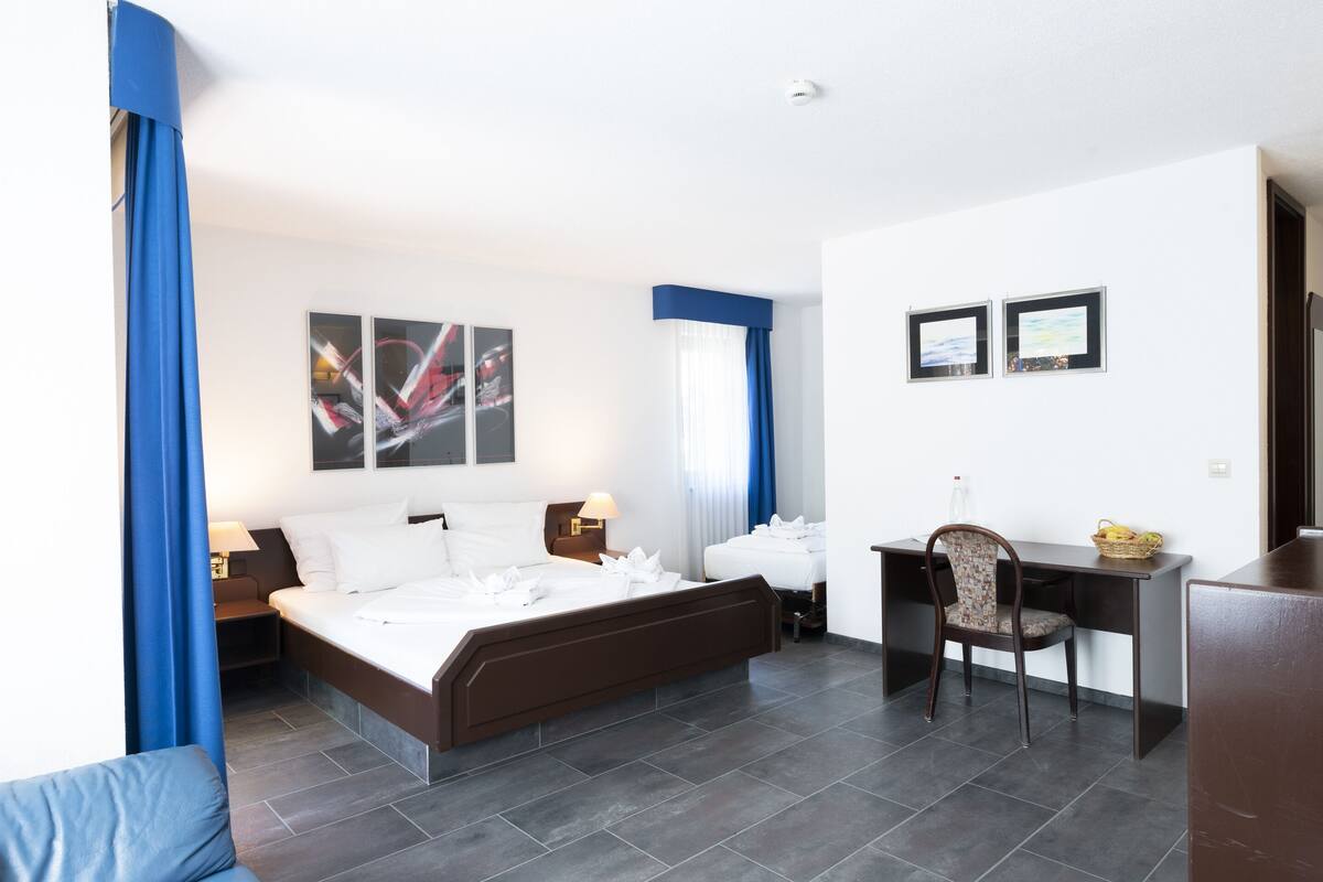A hotel room with a large bed, a desk, and a chair. There are two framed pictures on the wall.