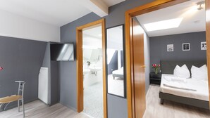 A modern hotel room with a bed, a TV, a desk, and a bathroom visible through a glass door. - Hotel Astoria am Urachplatz (Stuttgart)
