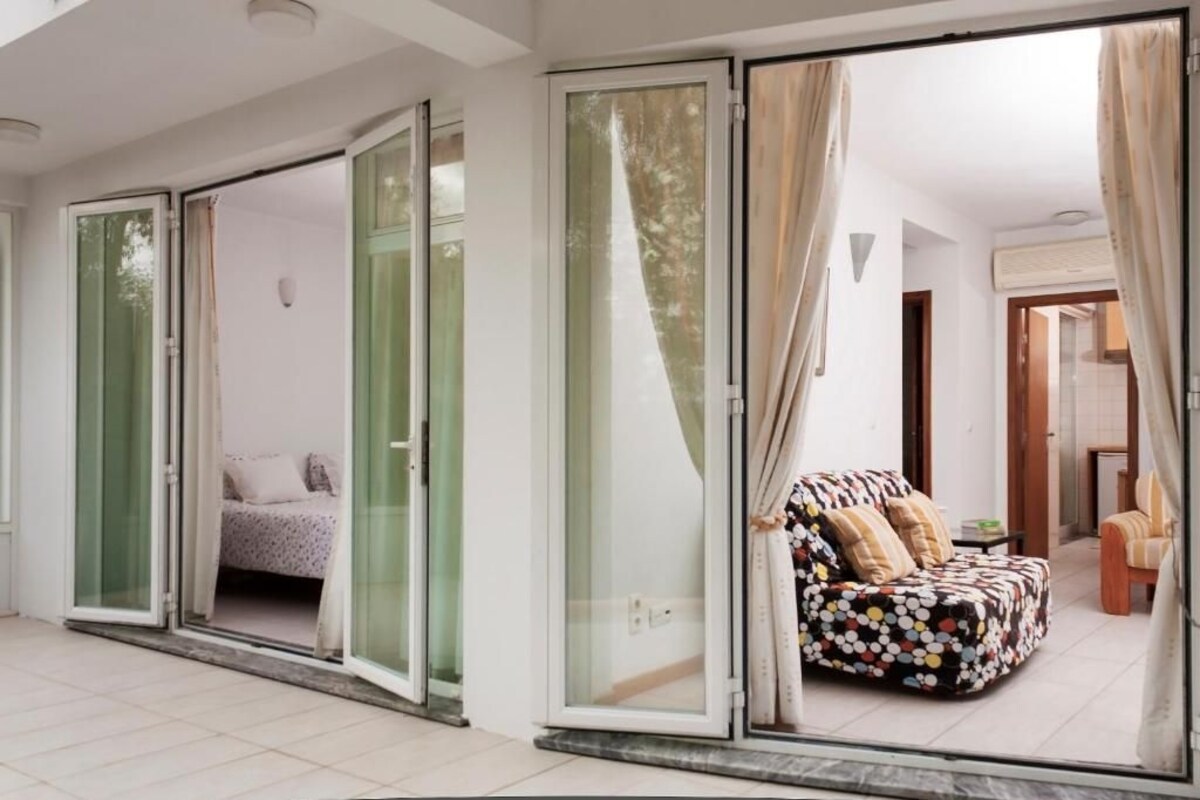 Una sala de estar moderna con sofá y cama, puertas de vidrio correderas que dan a un balcón y vistas al exterior.