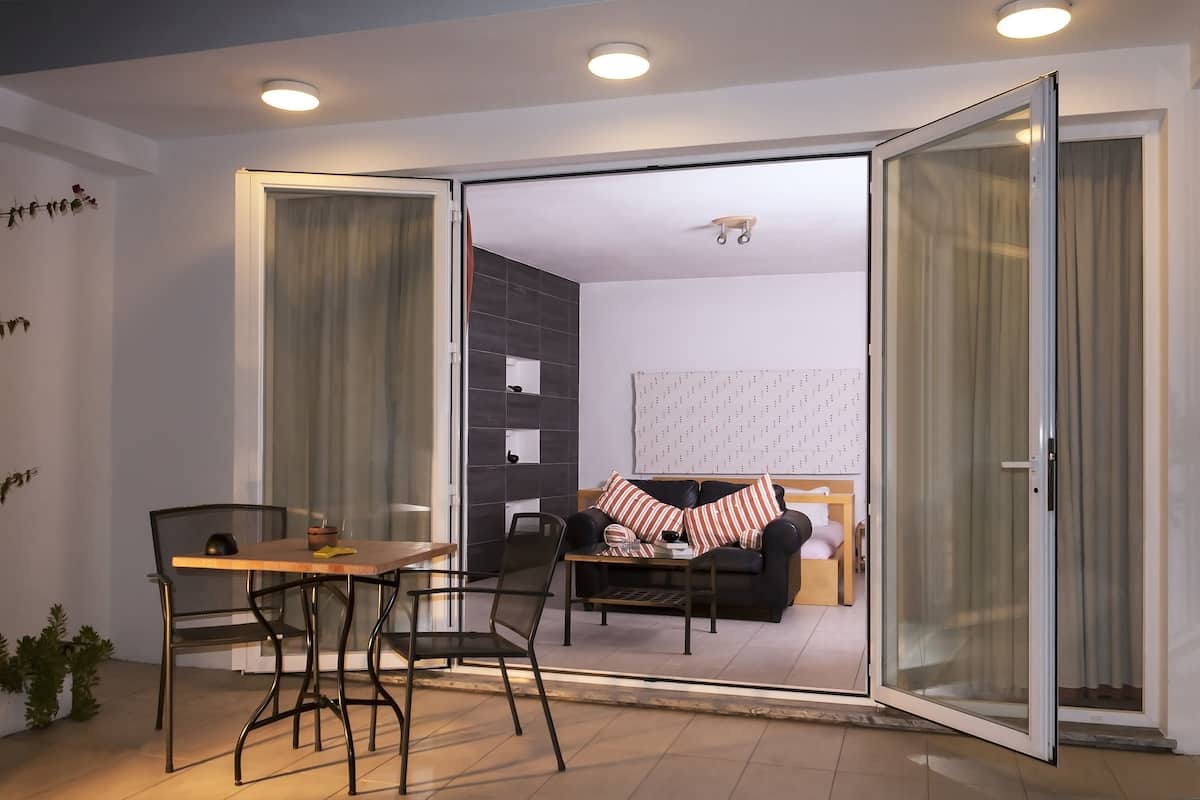 A modern living room with a sofa, a dining table with chairs, and a sliding glass door leading to another room.