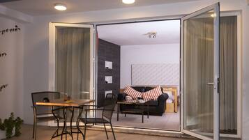 Una sala de estar moderna con un sofá, una mesa de comedor con sillas y un gran ventanal corredizo que da a otra habitación.