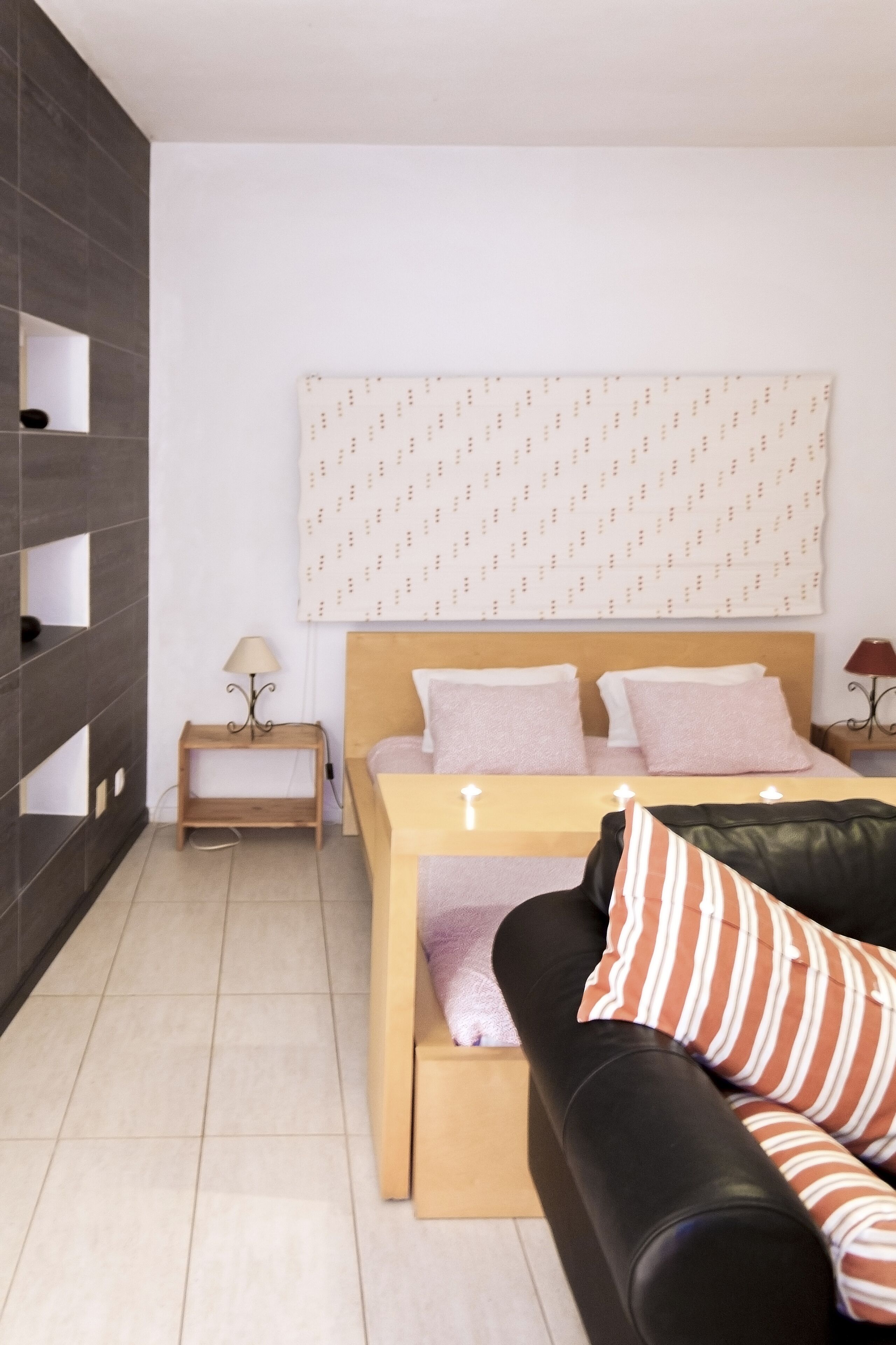A modern bedroom with a bed, a wooden nightstand, a black leather couch, and a patterned headboard.