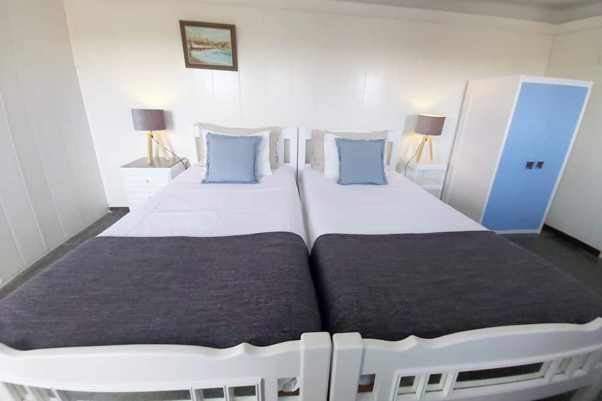A double bed with two pillows, a bedside table with a lamp, a wardrobe, and a framed picture on the wall.