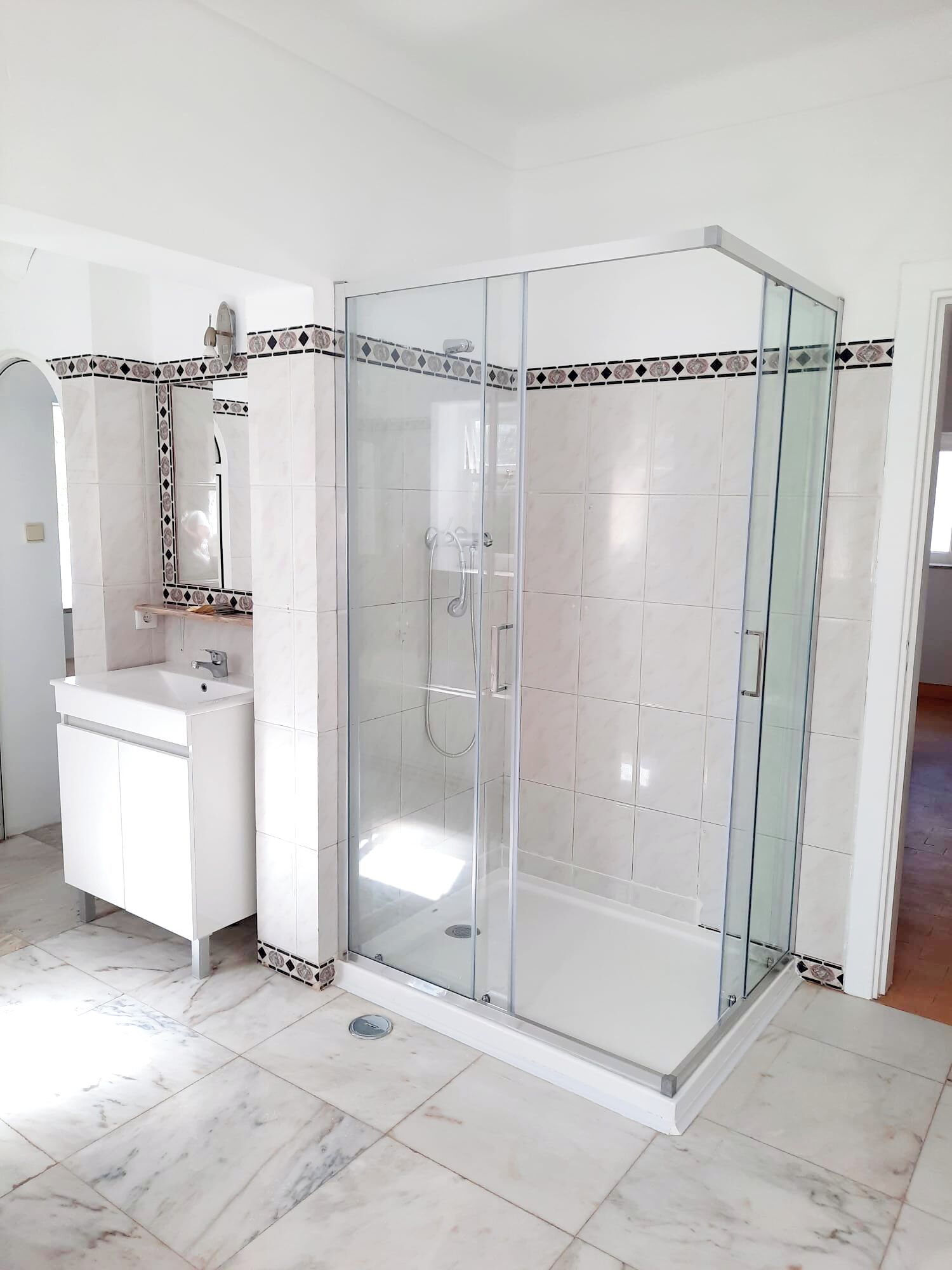 A modern bathroom with a glass-enclosed shower, a white sink, and a tiled floor.