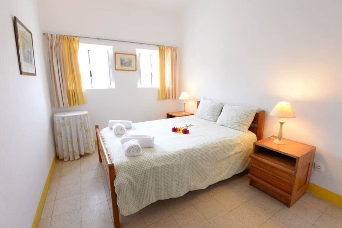 A bedroom with a bed, two bedside tables, a radiator, and curtains.