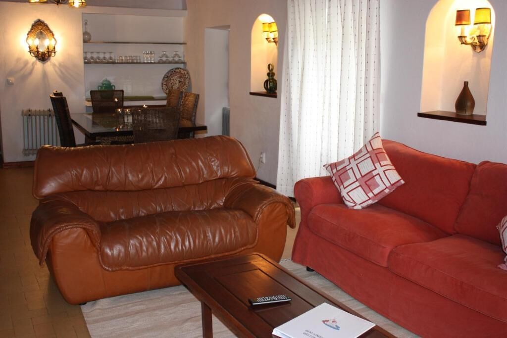 Un salon avec un canapé en cuir marron et un canapé rouge, une table basse et, au fond, un coin repas.