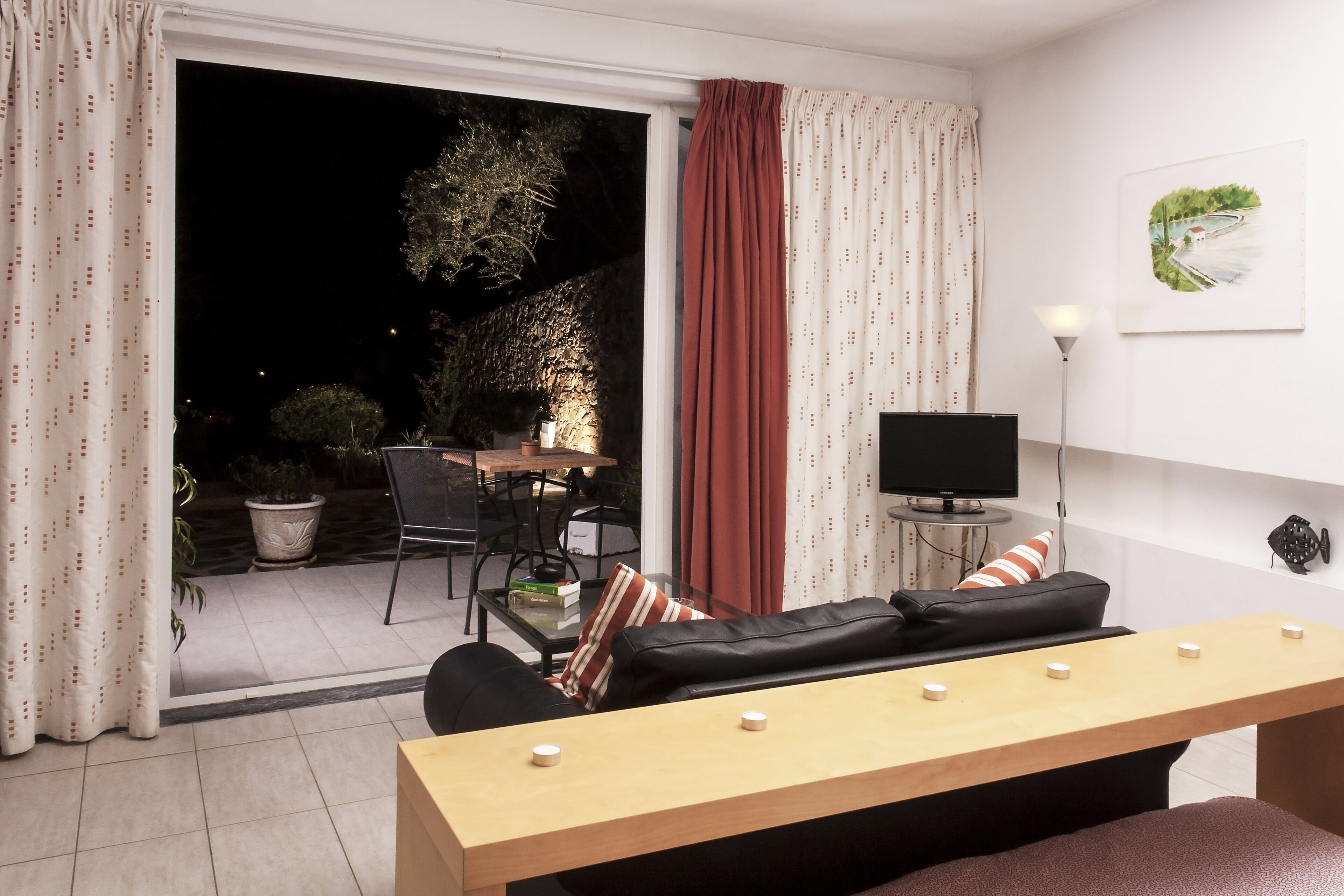 A modern living room with a sofa, a wooden table, a TV, and a view of the outside.