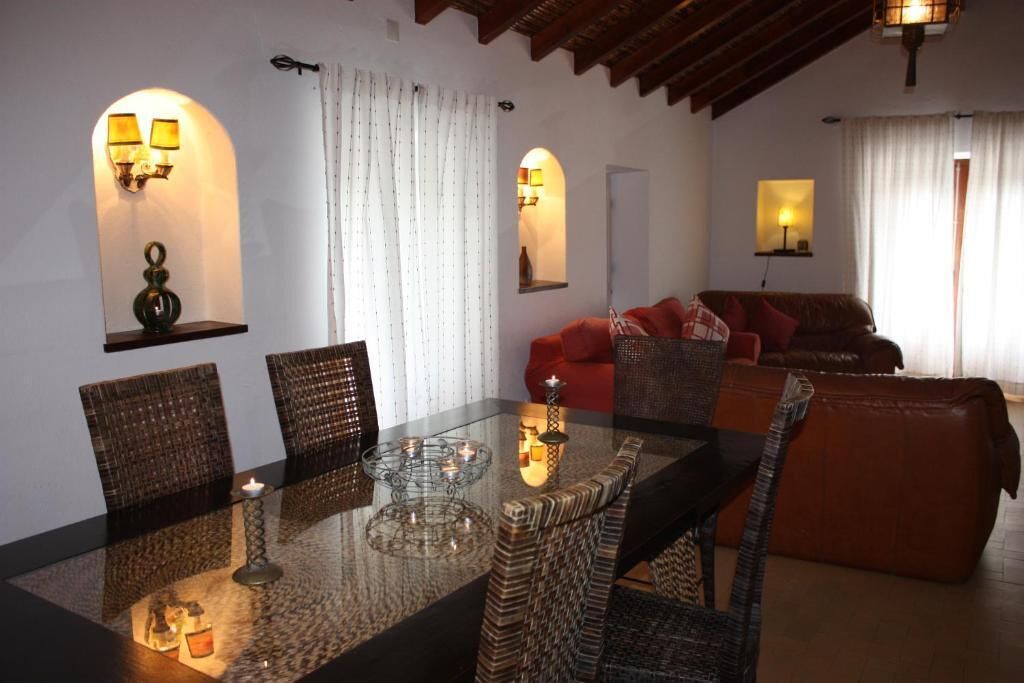 A dining area with a glass table, wicker chairs, and wall-mounted lamps.