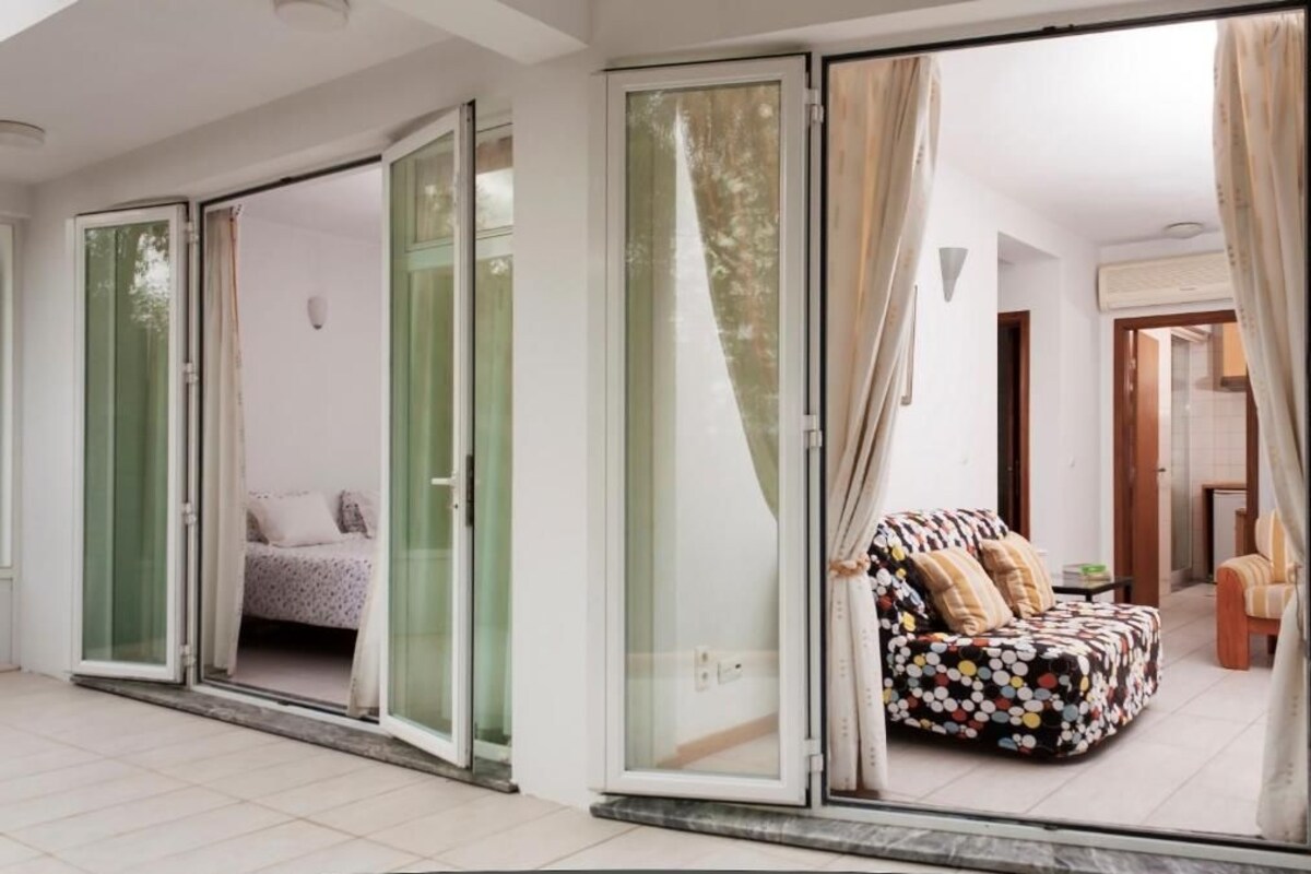Una sala de estar moderna con sofá y cama, puertas de vidrio correderas que dan a un balcón y vistas al exterior.