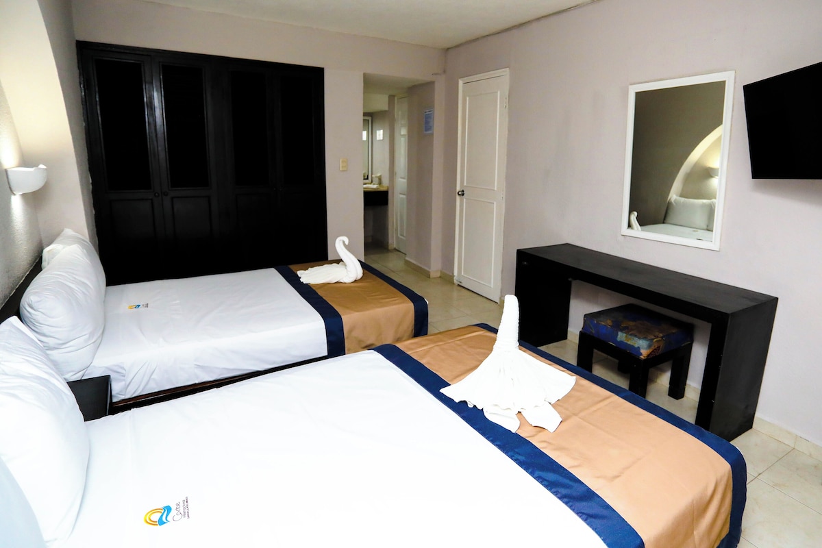 A hotel room with two beds, a desk, a chair, a mirror, and a door leading to a bathroom.