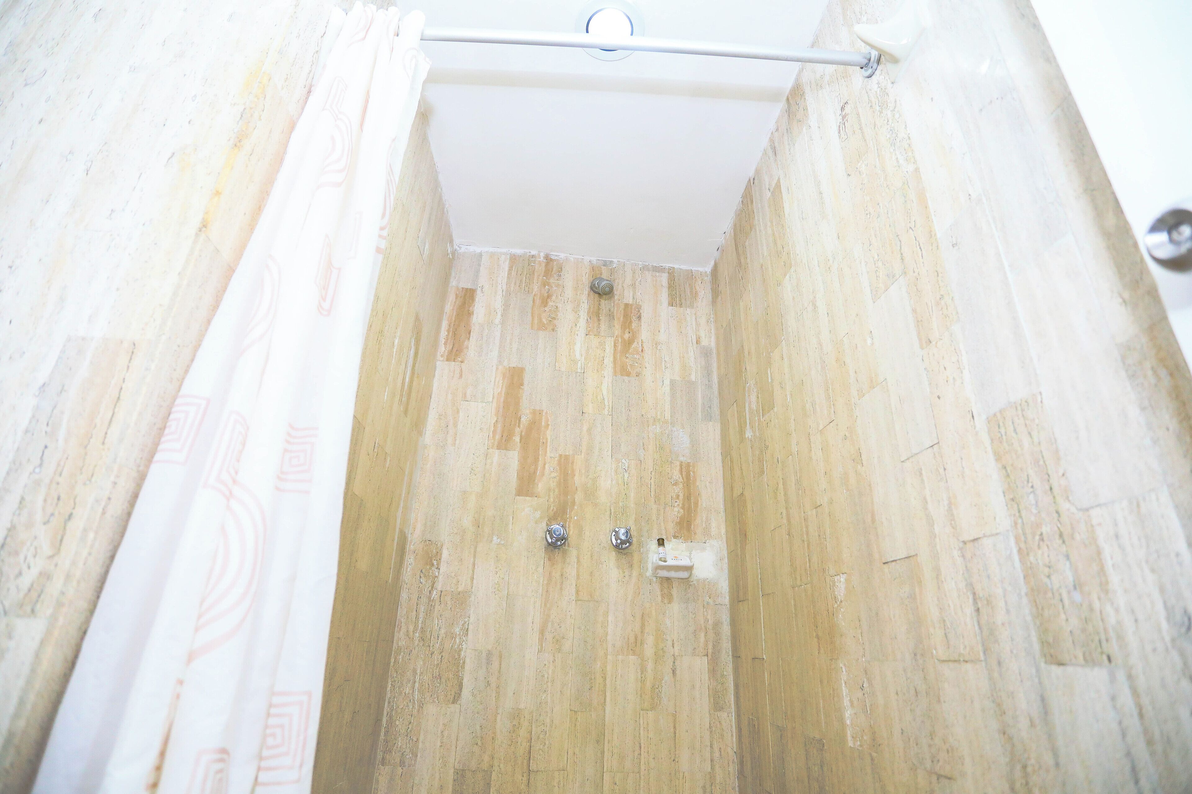 Ducha con piso de madera, techo blanco y barra de cortina metálica.