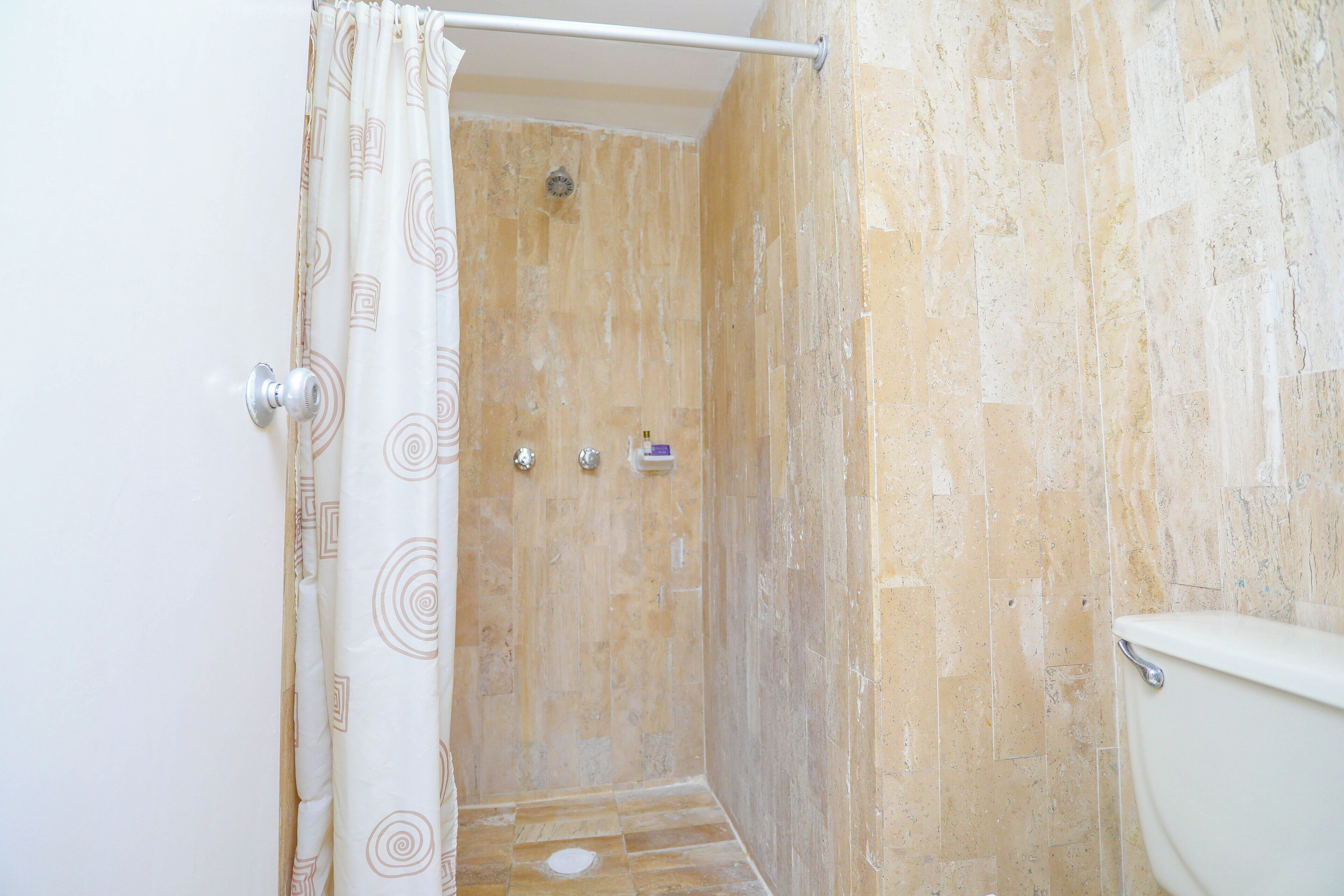 Une salle de bain avec une douche, des toilettes et un mur agrémenté d’un rideau de douche à motifs.