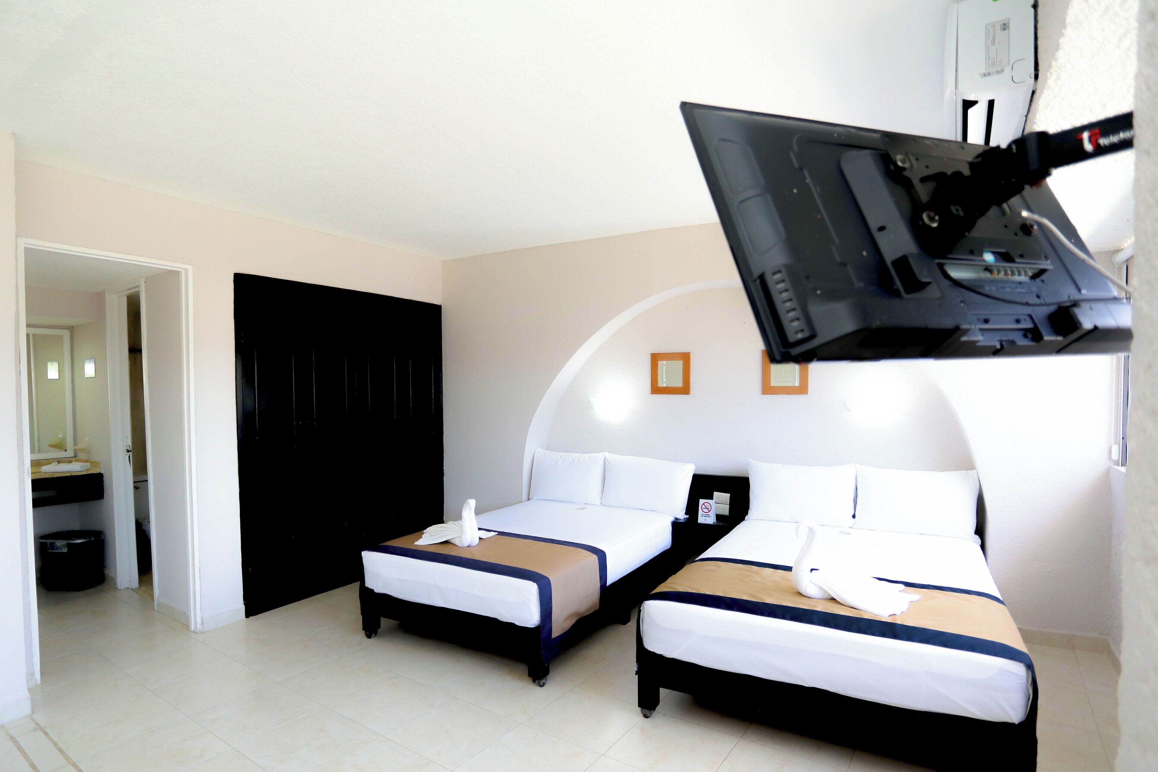 Une chambre d’hôtel avec deux lits, une armoire noire, une petite salle de bain et un téléviseur fixé au mur.