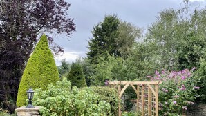 A garden with a stone wall, a wooden pergola, and various plants. - Plumpton Court (York)
