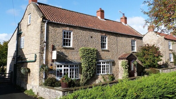 A stone building with a tiled roof, a small porch, and a sign indicating a restaurant. - Plumpton Court (York)