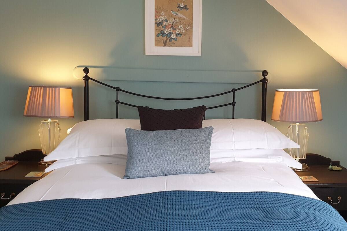 Un lit bien fait, recouvert d’une couverture bleue, avec deux oreillers et une œuvre d’art encadrée au-dessus.