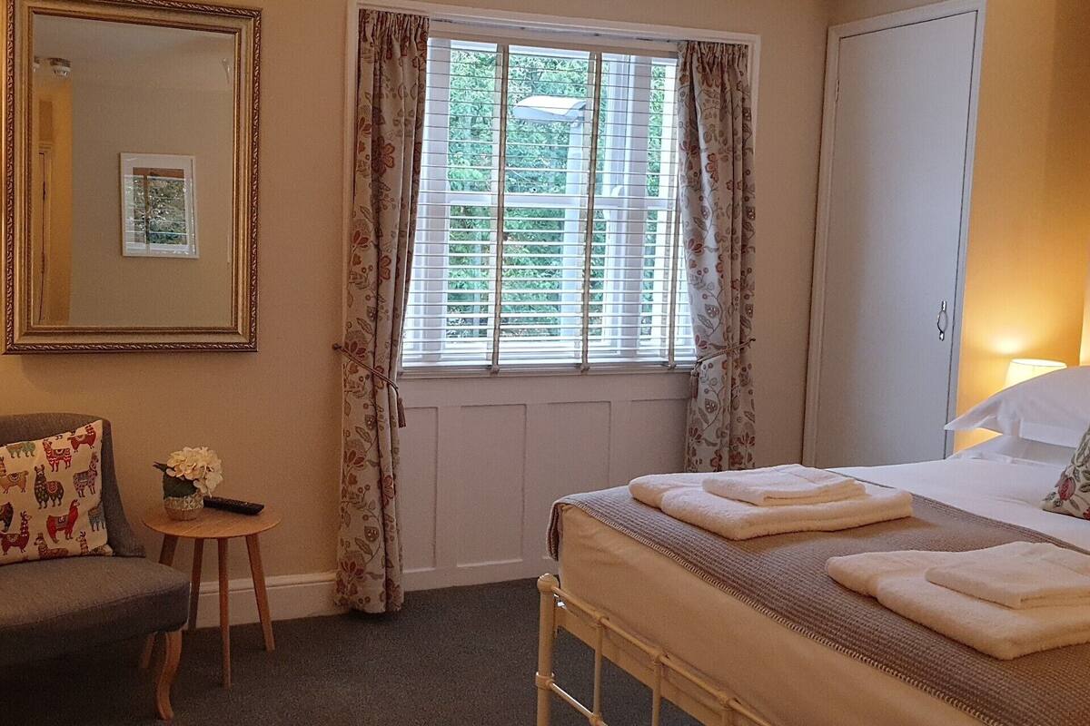 Une chambre à coucher avec un lit, une table de chevet, une chaise, une fenêtre avec des rideaux et un miroir.