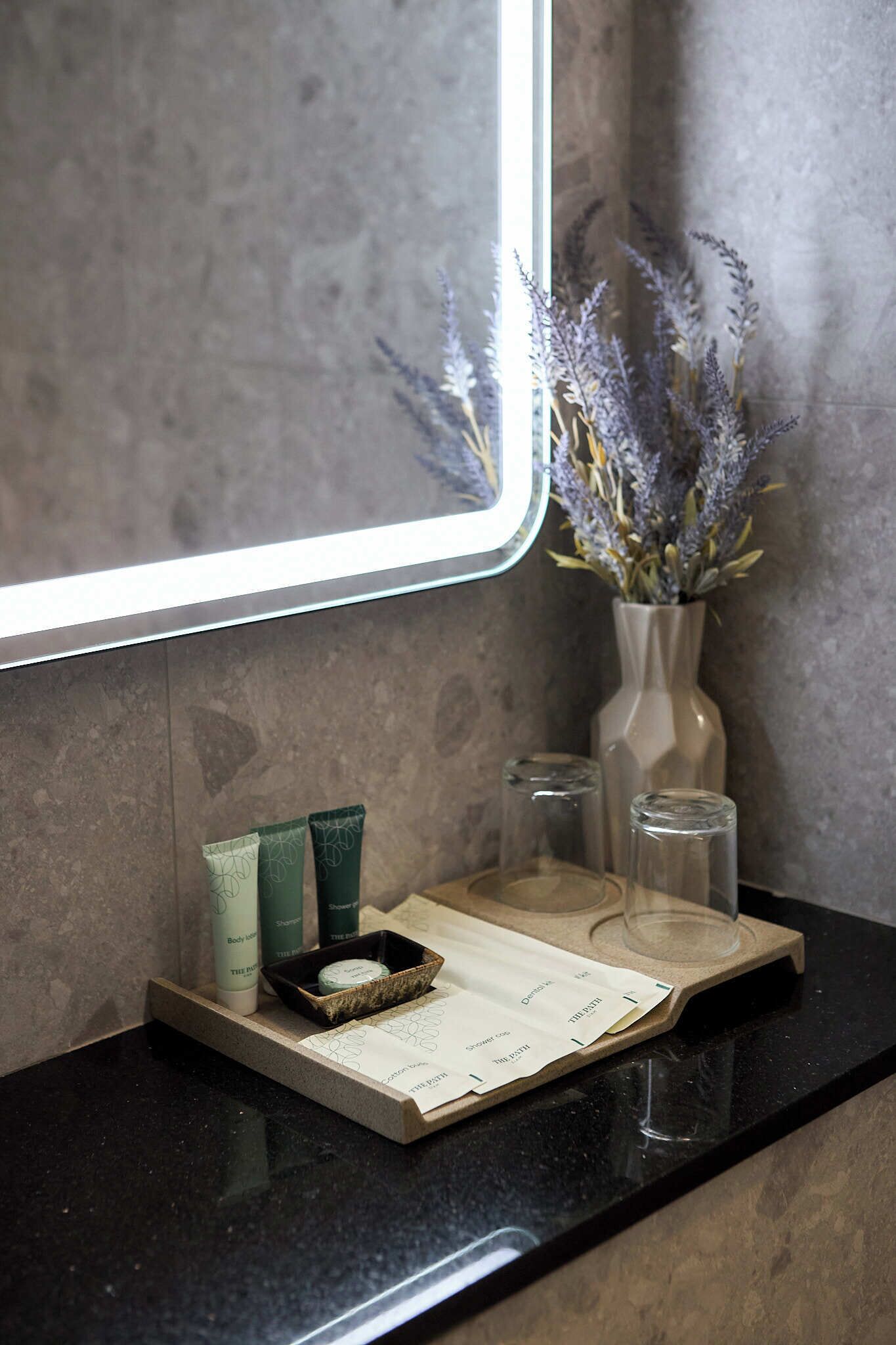 Un mobile bagno con uno specchio, un vaso di lavanda e articoli da toilette su un vassoio.