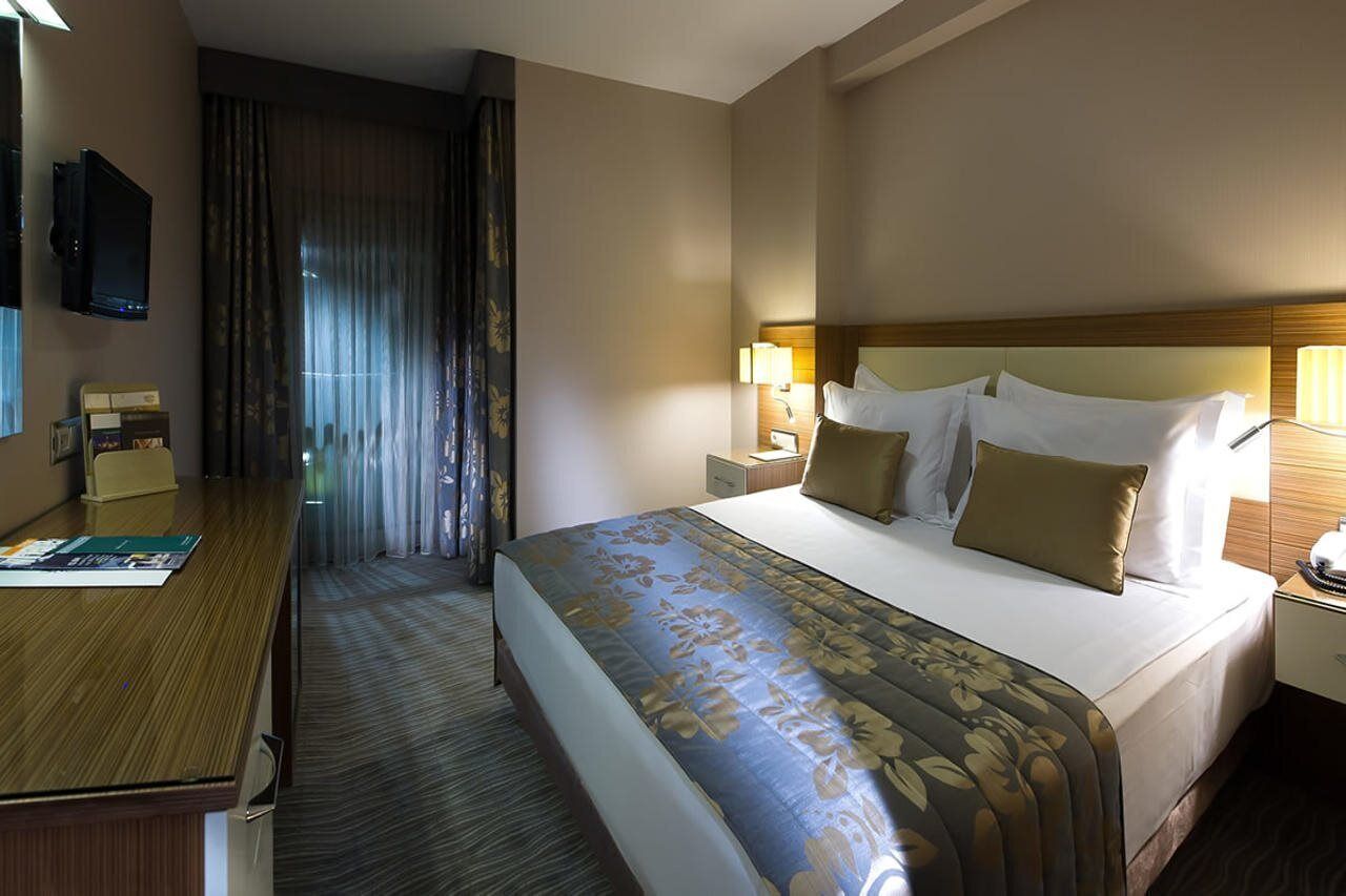 A hotel room with a large bed, a desk, a television, and a window with curtains.