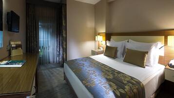 A hotel room with a large bed, a desk, a television, and a window with curtains.