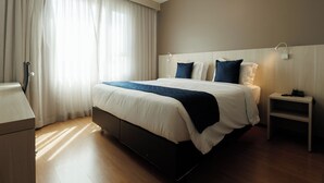 Una habitación de hotel moderna con una cama grande, una mesita de noche y otra mesita auxiliar.